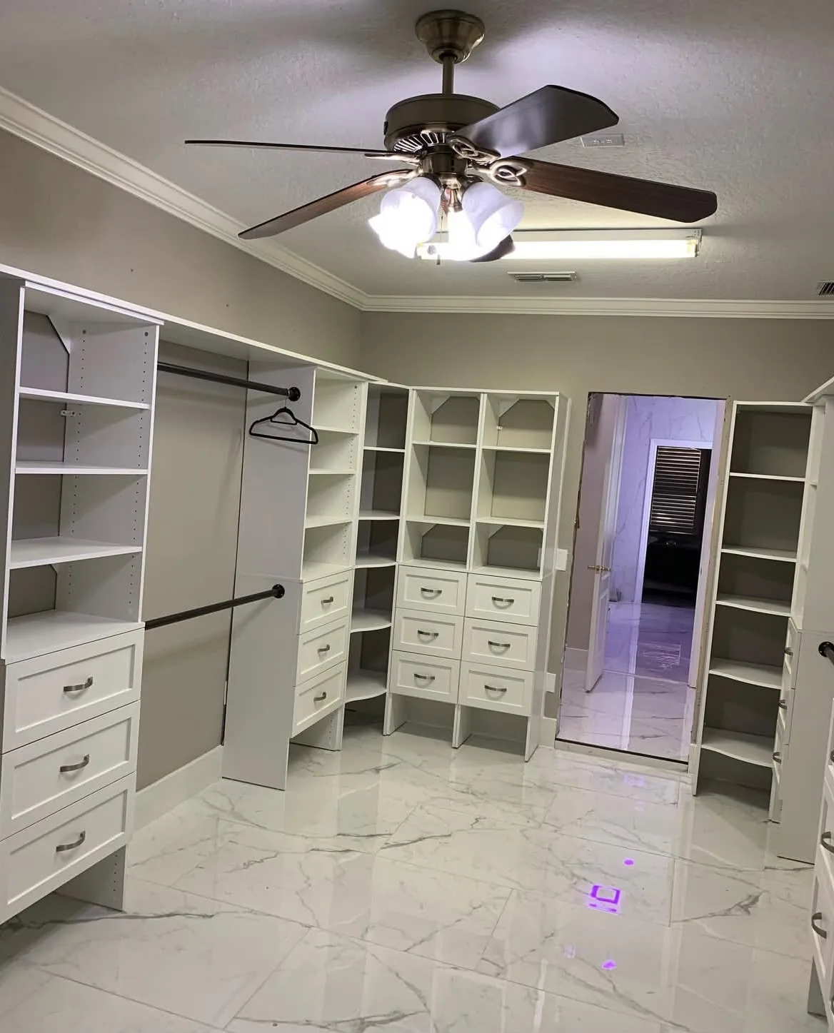 Finished walk-in closet with custom white cabinetry and marble-look tile flooring